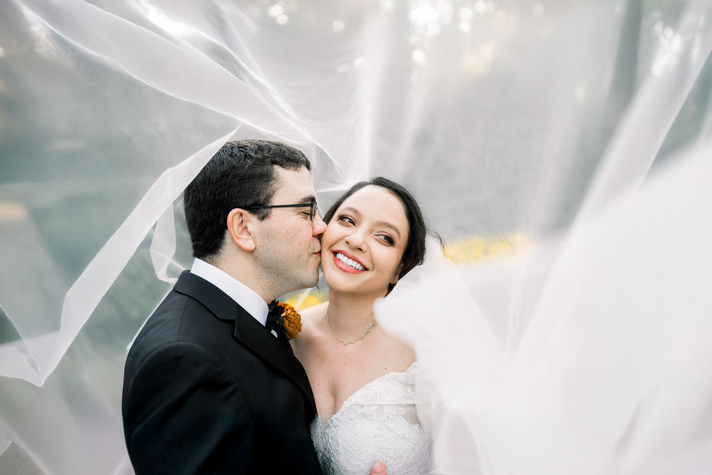 Groom kissing bride on the cheek while veil flies over their heads at The Mazant in the Bywater of New Orleans
