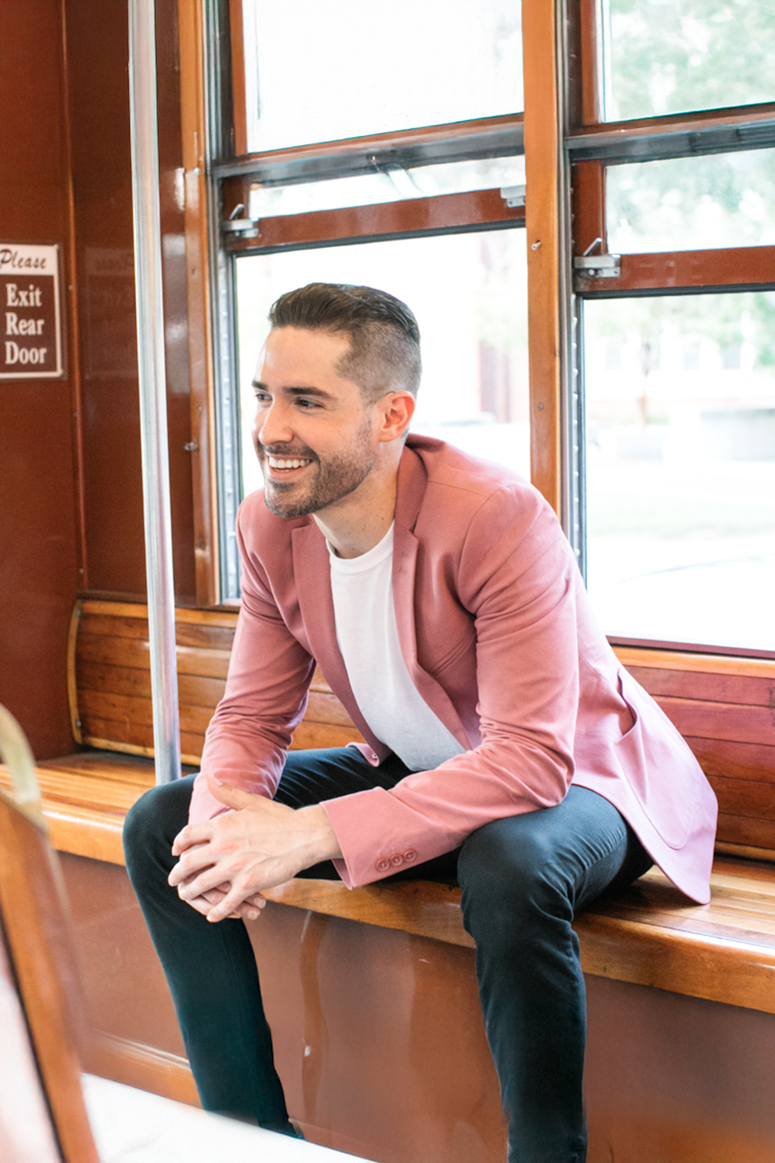 Ryan H Gray, owner of Moment Makers Photography, riding a street car in New Orleans and looking fashionable in pink blazer and black pants