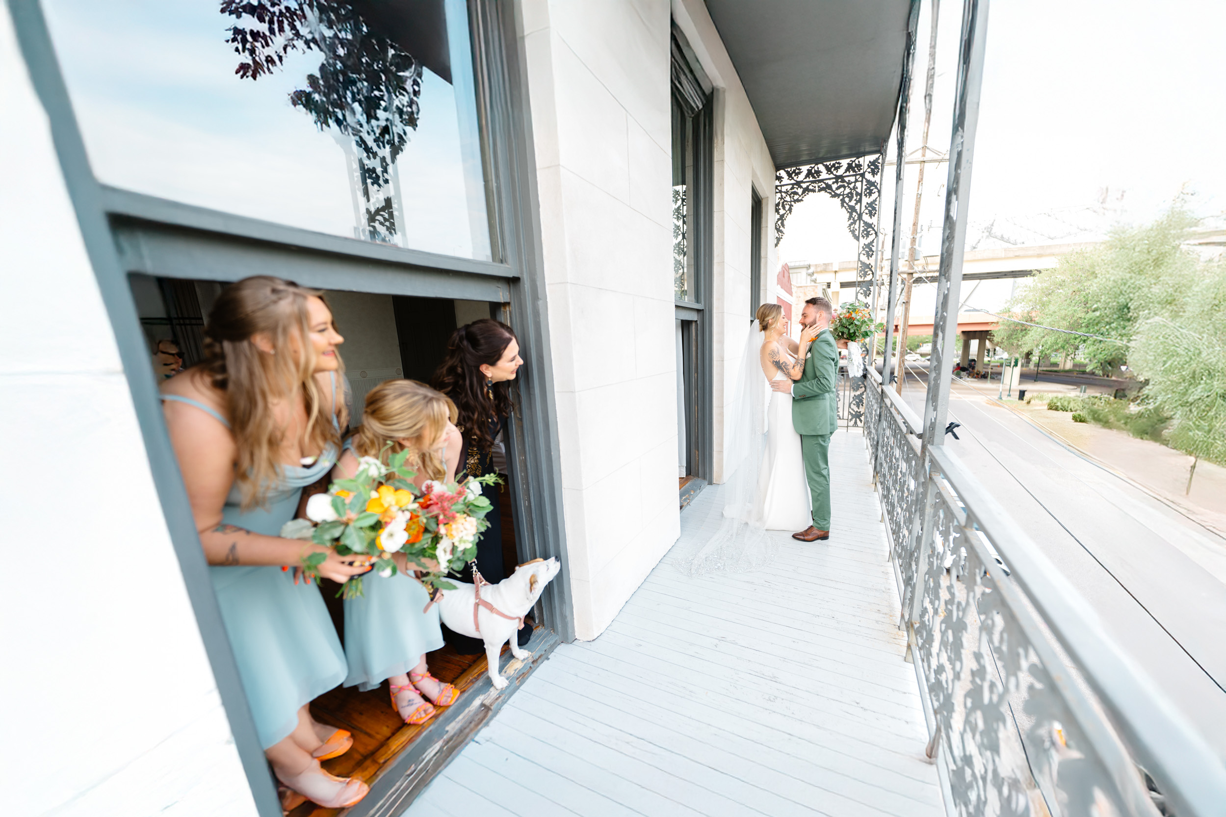 bride and groom kissing during their first look on balcony while bridesmaids watch at Margaret Place in New Orleans
