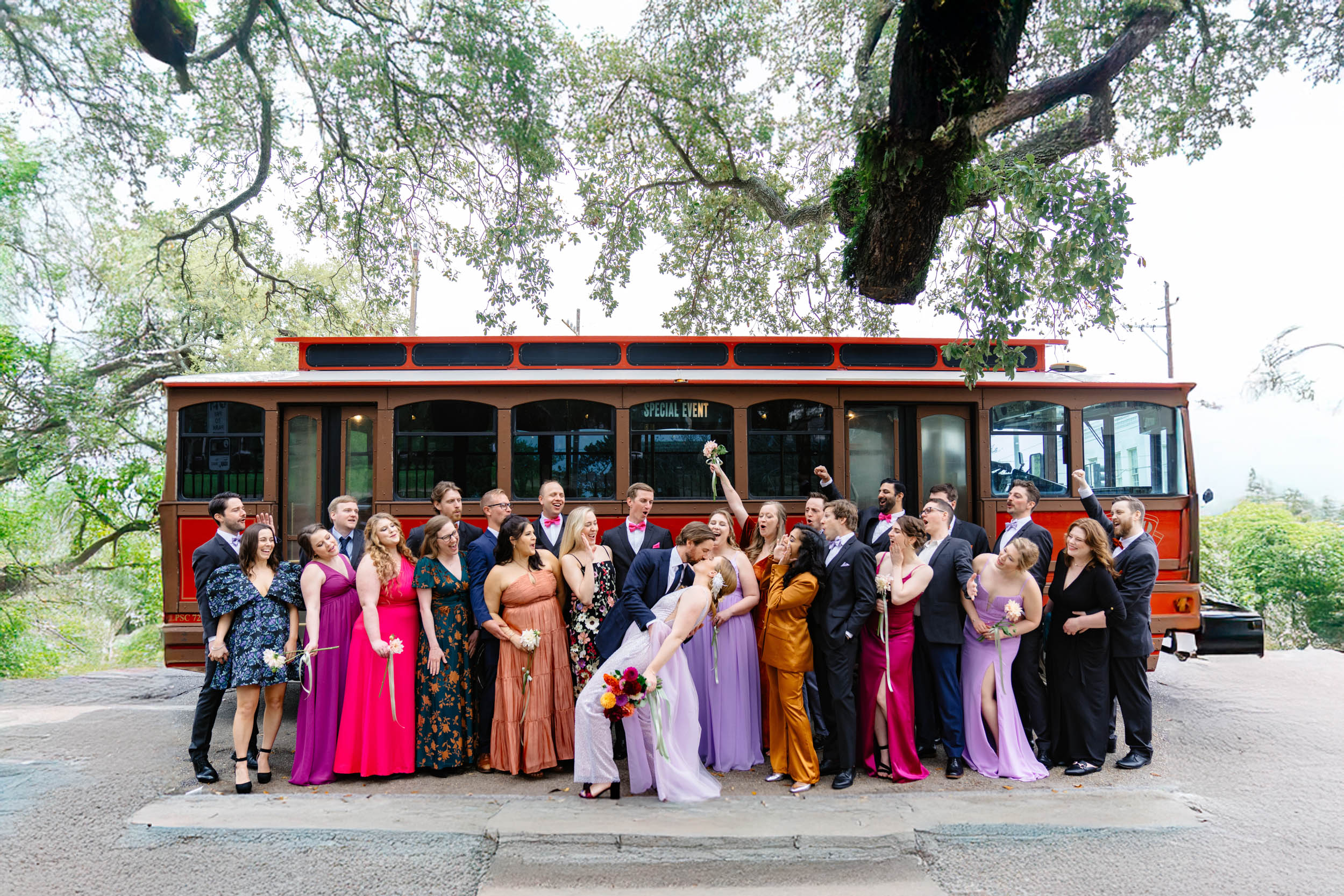 bride and groom kissing next to wedding party in front of trolley in the New Orleans Bywater at Washington Square Park