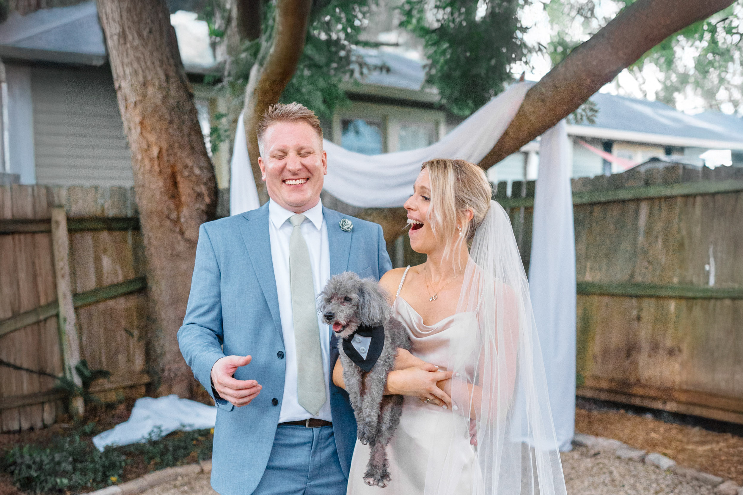 bride and groom laughing while holding their dog in backyard wedding in uptown New Orleans
