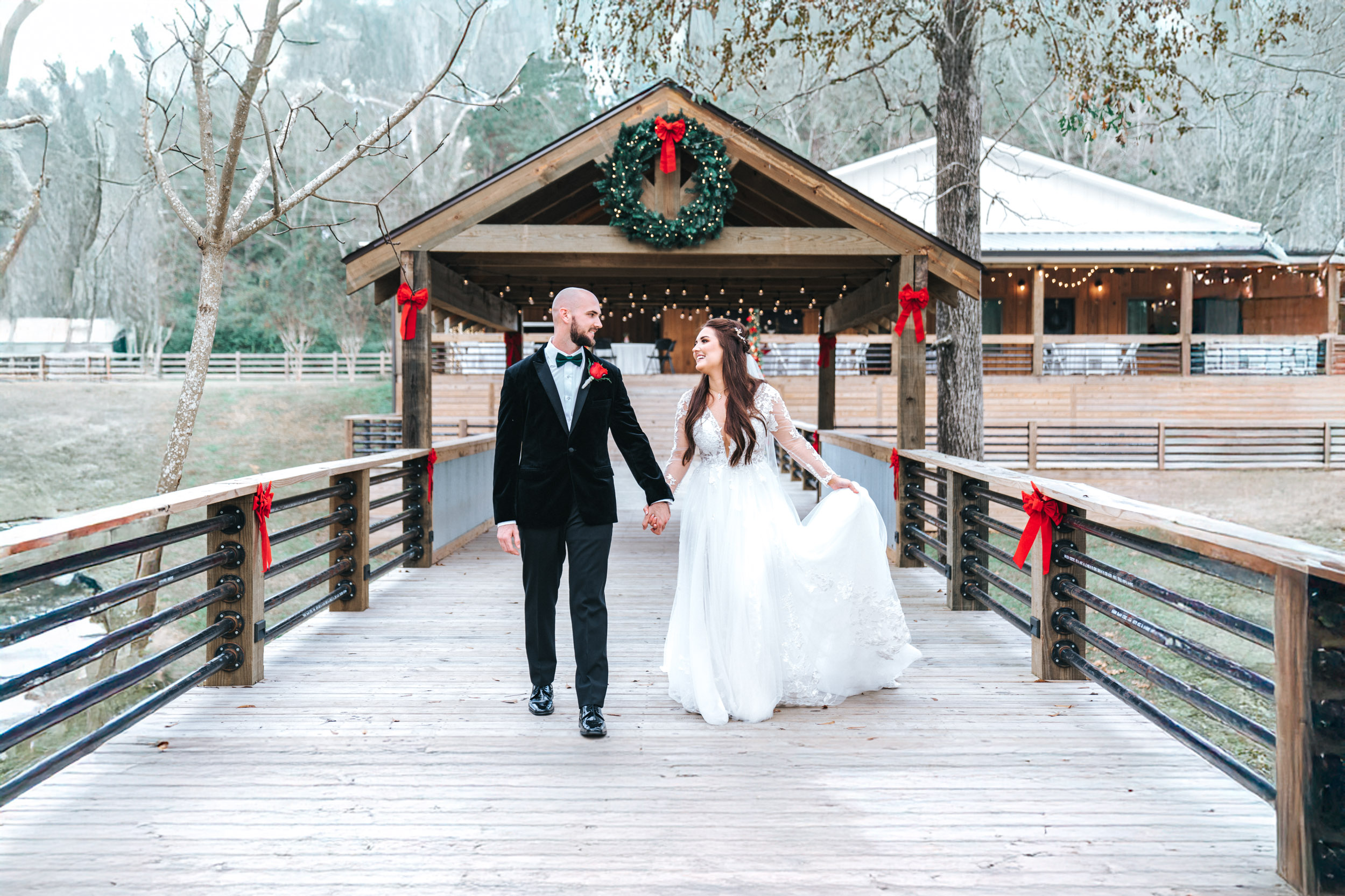 bride and groom walking together on bridge over a creek with Christmas theme and wreaths at Creekview Barn in Mississippi