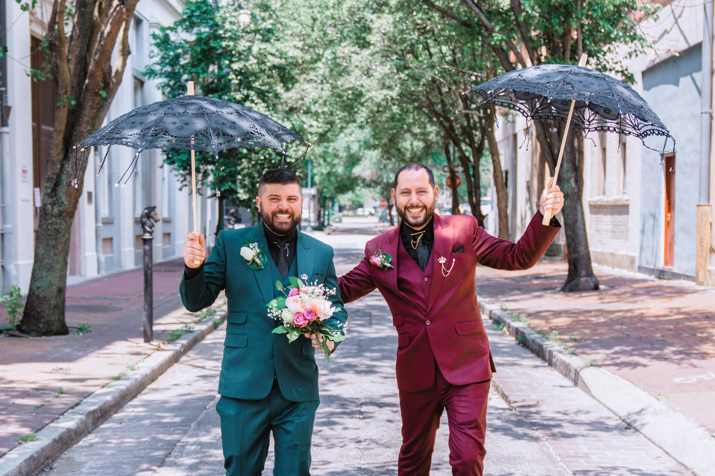 gay couple laughing in street with umbrellas for their elopement in New Orleans